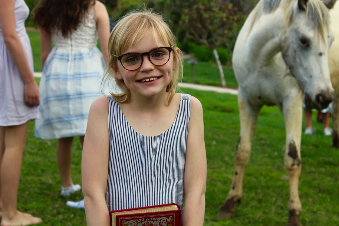Mädchen mit Brille neben einem weißen Pferd